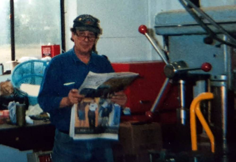 FL Decker wearing a hat and reading a newspaper in a machine shop